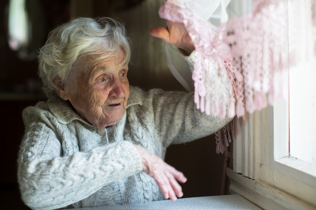 Elderly woman looks mildly confused as she looks out the window.