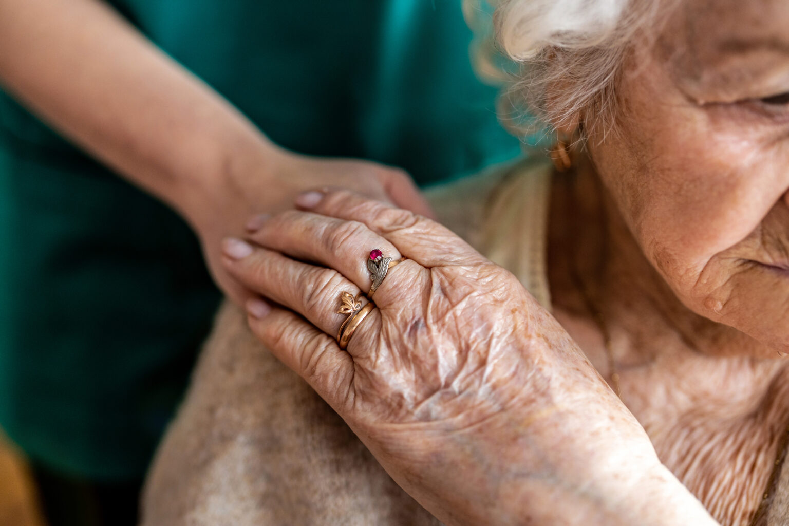 An elderly woman is comforted with a hand on the shoulder